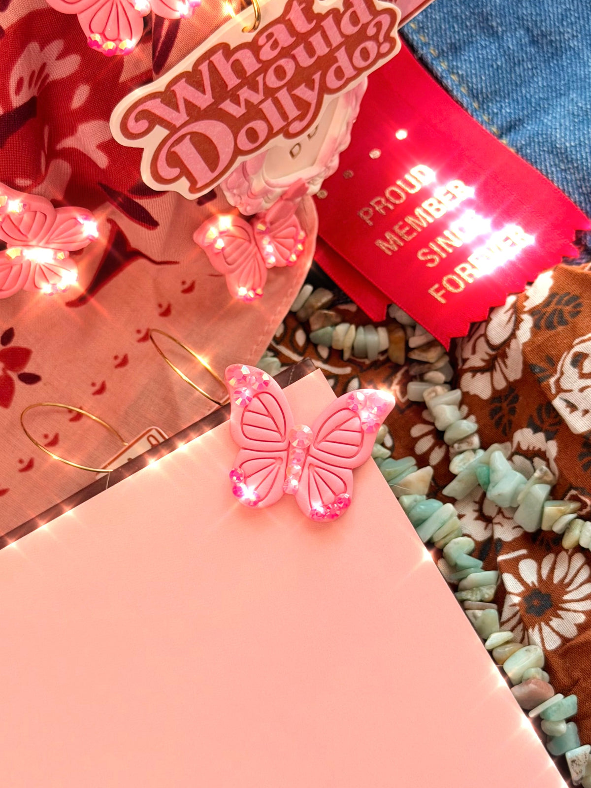 Pink rhinestone butterfly corner bookmark clipped onto a pink book with Dolly Collection accessories in the background