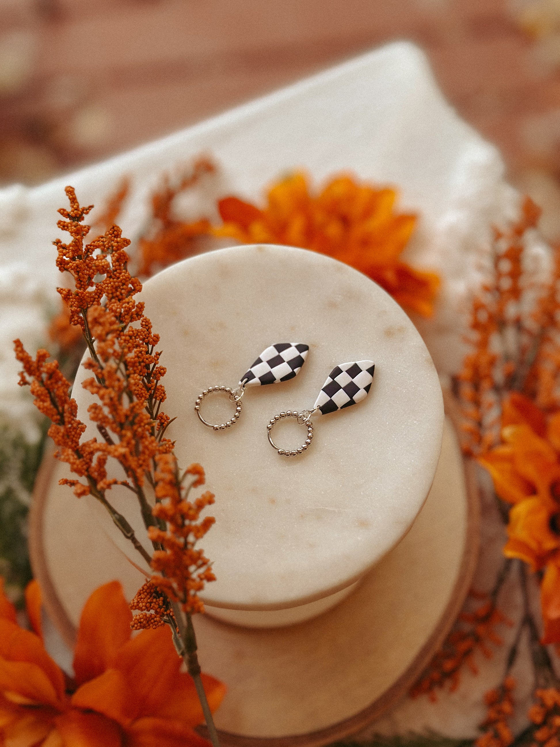 Pair of checkered earrings on a white stone surface with orange flowers in the background