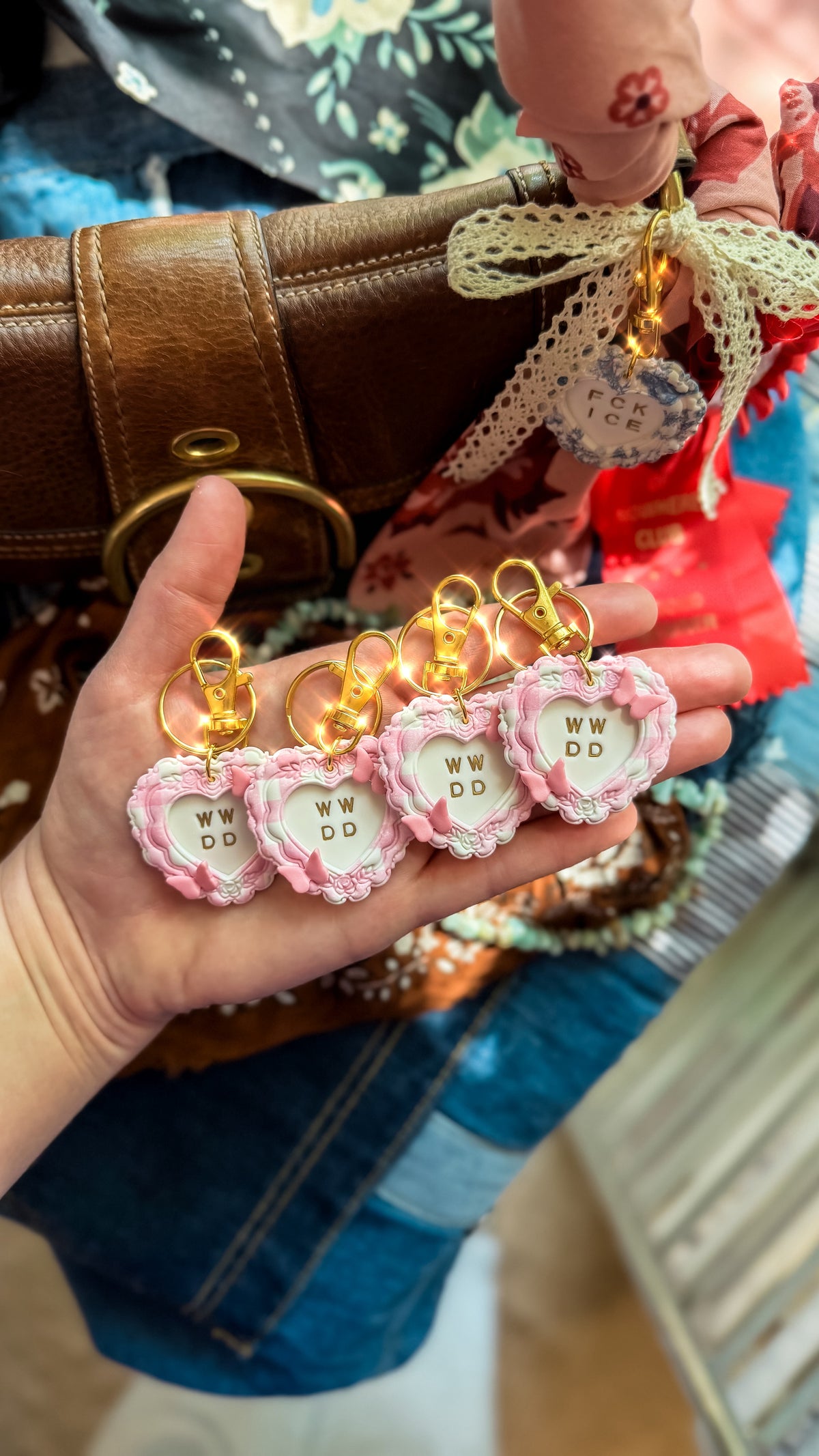 Four handmade What Would Dolly Do pink heart keychains with gold hardware displayed in hand beside a brown purse