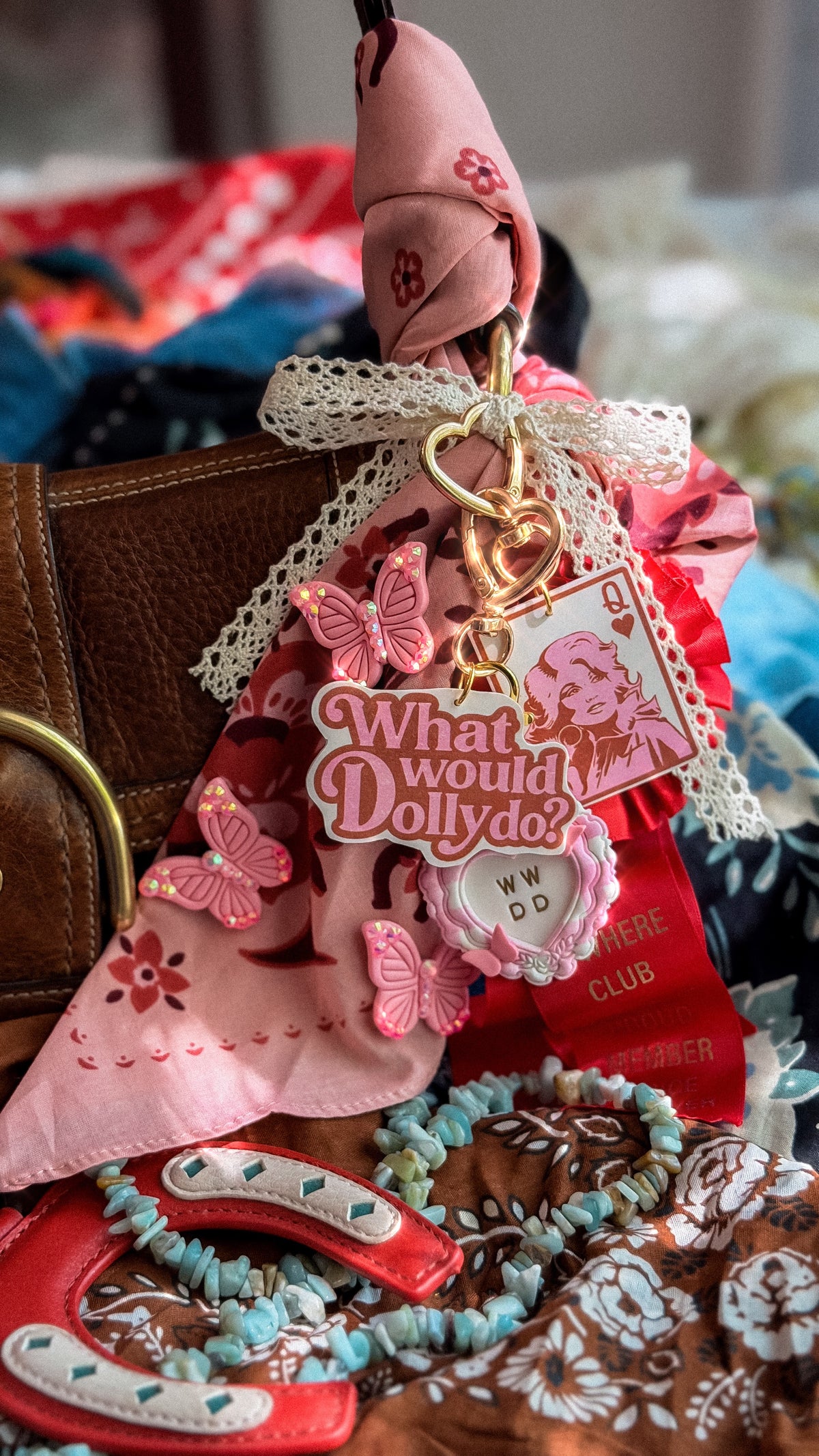 Pink Dolly Parton-inspired What Would Dolly Do keychain styled on a purse with rhinestone butterflies and western accessories