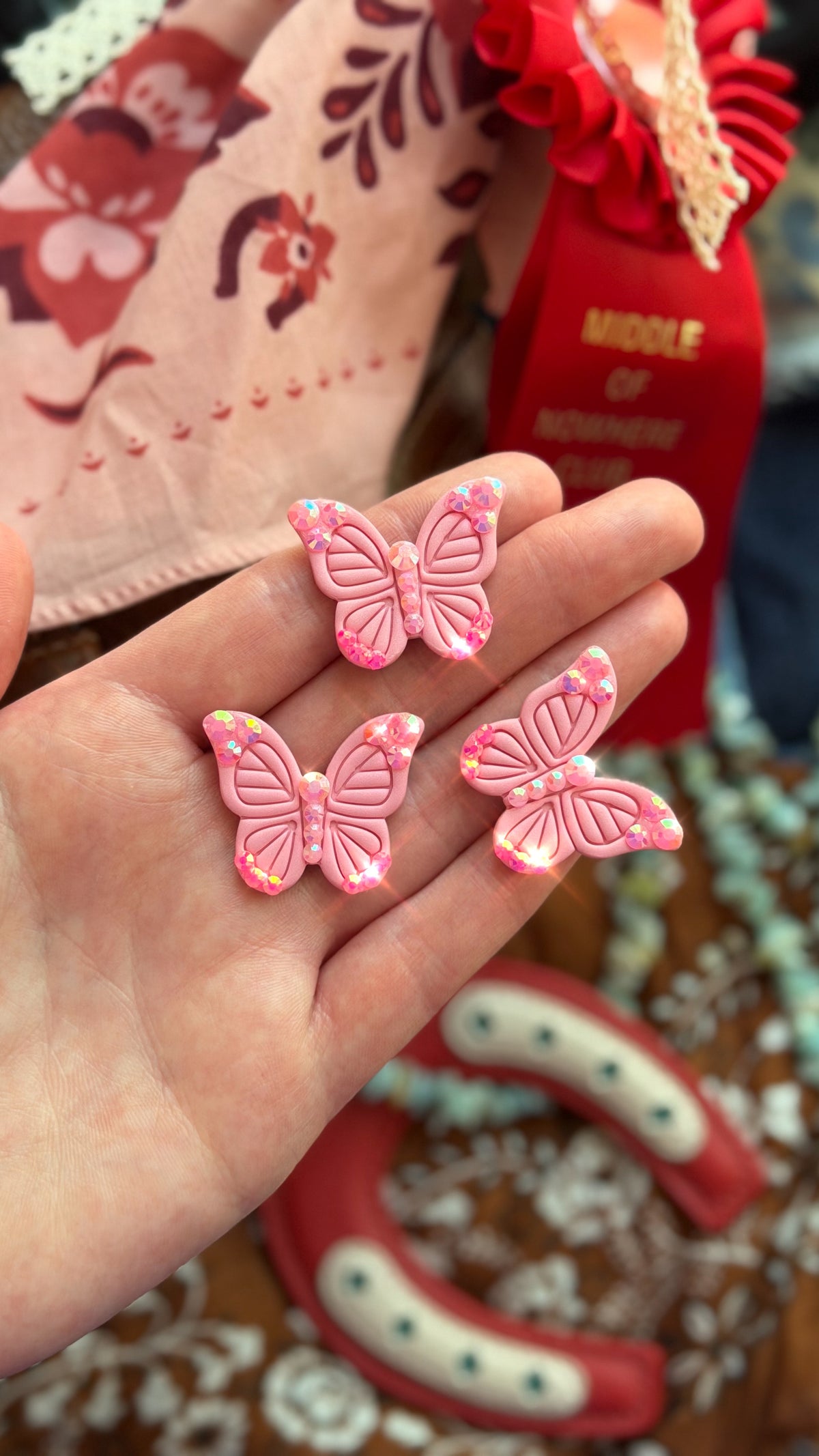 Three sparkly pink butterfly pins displayed in hand with colorful western accessories in the background