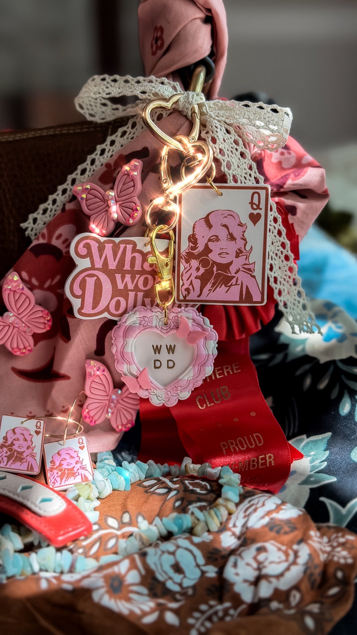 Dolly Parton-inspired Queen of Hearts bag charm with gold hardware beside WWDD heart and butterfly accessories