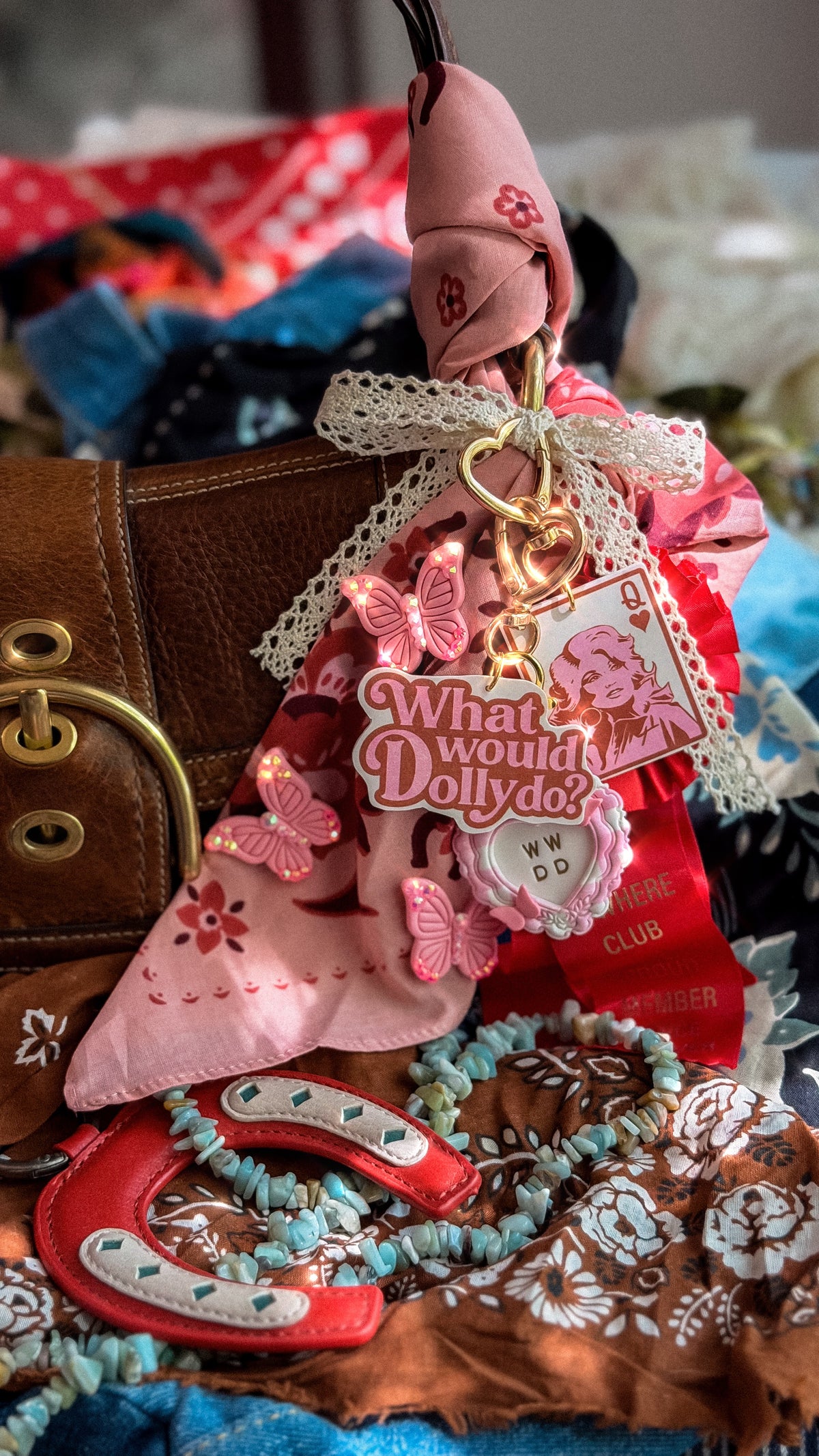 What Would Dolly Do bag charm and keychain clipped to a brown leather purse with pink floral scarf and lace ribbon