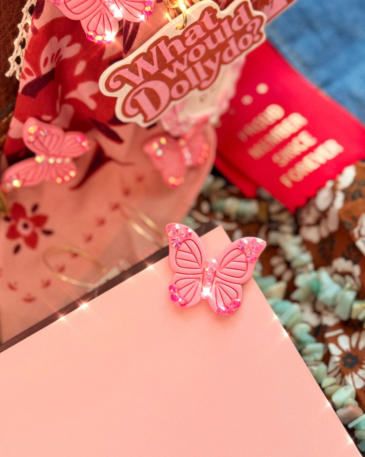Sparkly pink butterfly bookmark clipped onto the corner of a book beside What Would Dolly Do accessories